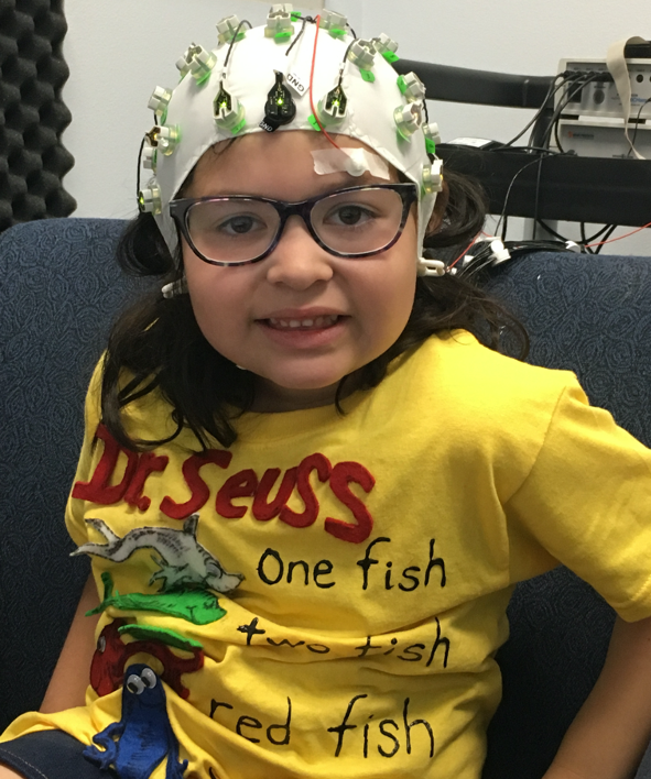 A child with glasses wearing an EEG cap in the Social Cognitive Neuroscience Lab. 
